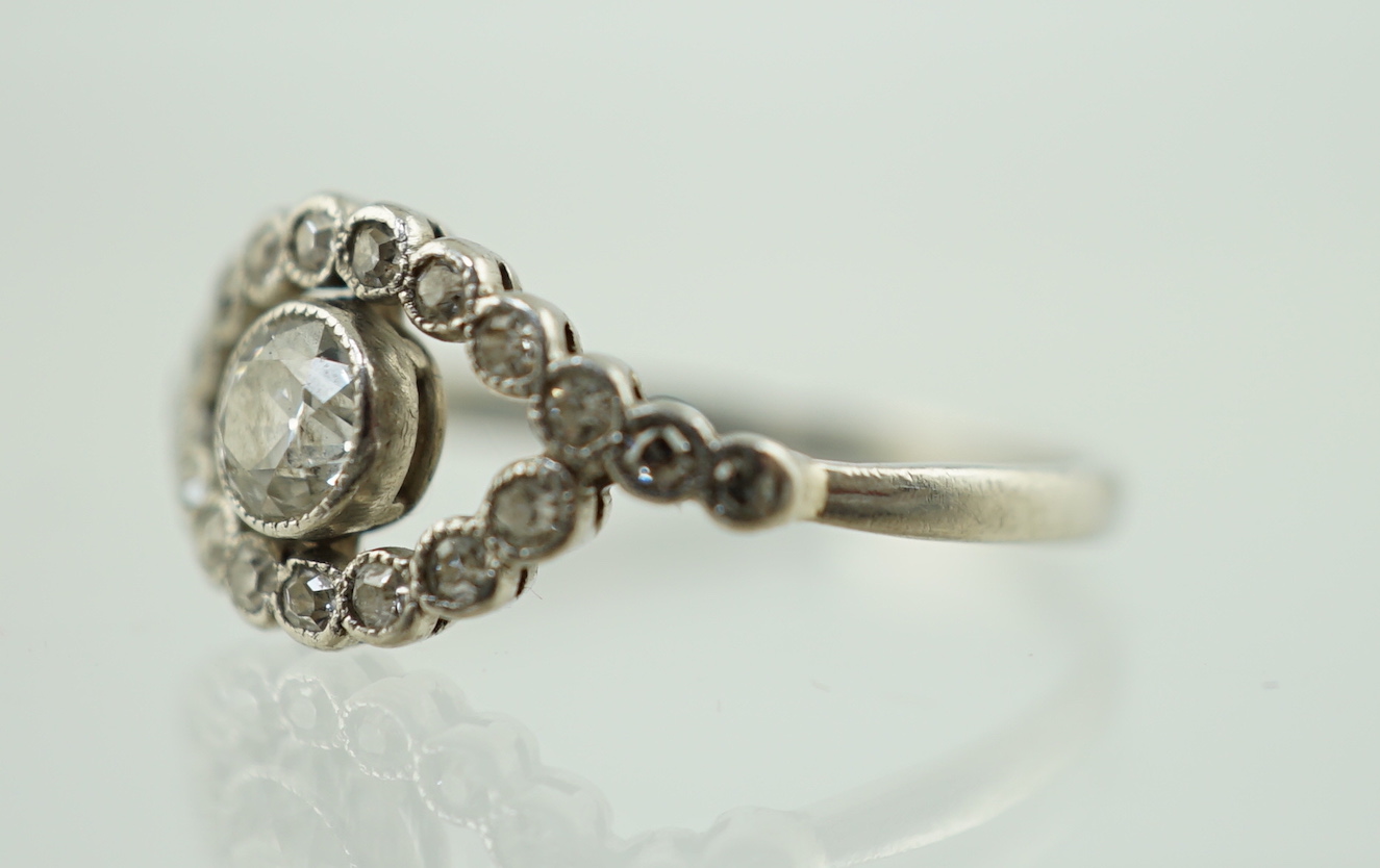 A white metal and single stone elliptical shaped ring, with diamond set border and shoulders, size M, gross weight 2.1 grams.
